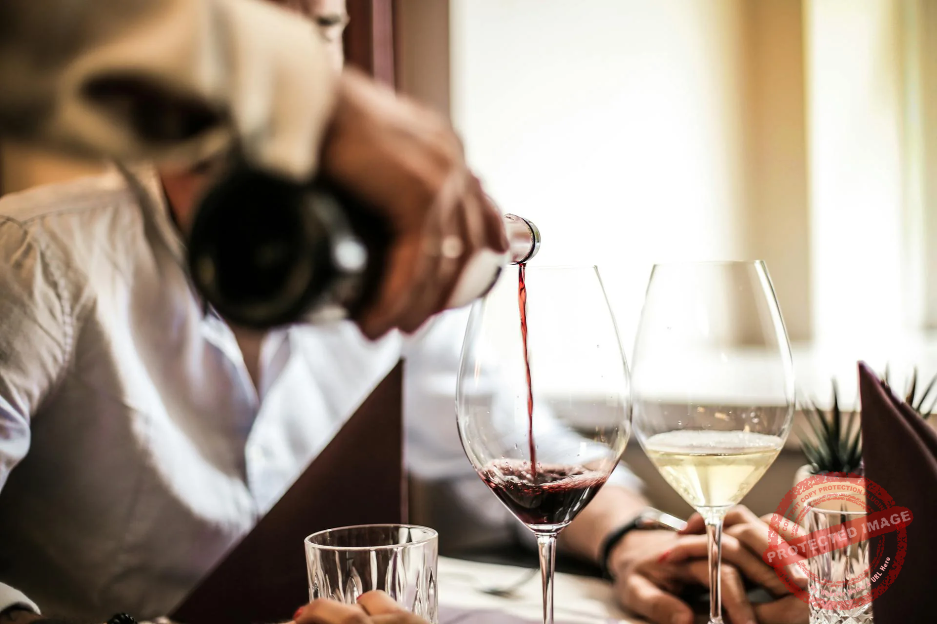 A waiter pouring a glass of wine for a couple in a nice restaurant